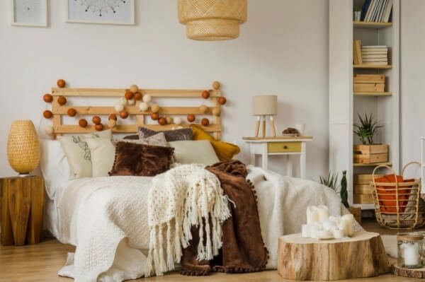 Dormitorio Boho decorado en tonos tierra y ocre con lámpara de mimbre sobre la cama y mesitas de noche de madera en estilo desigual